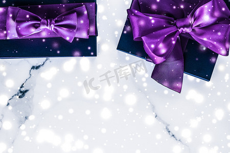 紫色的雪花摄影照片_冬季节日礼盒，配有紫色丝绸蝴蝶结、大理石背景上的雪花，作为豪华美容品牌的圣诞和新年礼物，平铺设计