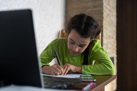 上学的摄影照片_戴耳机的微笑白人小女孩使用笔记本电脑与老师进行远程视频通话，快乐的小孩与导师挥手致意，在电脑上在线学习，在家上学的概念