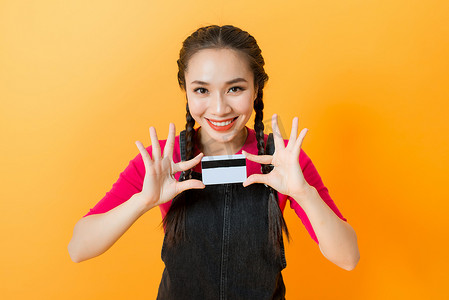 年轻微笑的美丽亚洲女性手持信用卡，表现出对付款的信任和信心