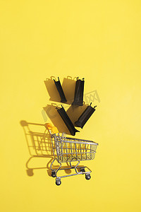 星期五黄色摄影照片_黄色背景黑色星期五销售中带购物袋的平躺式微型超市推车