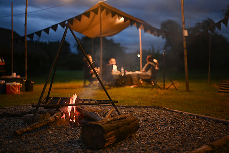 在附近摄影照片_晚上在户外露营帐篷附近篝火，人们坐在背景中。