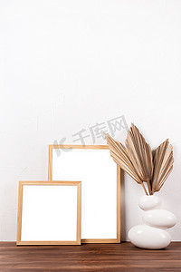 极简主义背景摄影照片_木桌上花瓶里有干棕榈叶的白色框架模型