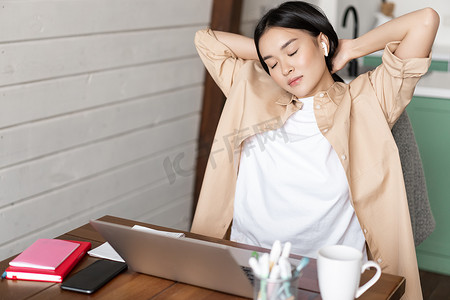 疲惫的亚洲女孩下班休息，在笔记本电脑上做作业后伸展手臂，坐在家里，在家远程工作或学习