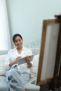 一位亚洲女性使用平板电脑在沙发上绘画艺术品的肖像。