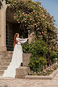一位穿着白色飘逸长裙的漂亮女人住在一片美丽的田野附近，那里有粉红色的花朵后视