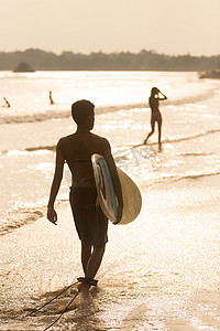 阳光下，一名男子手持冲浪板在斯里兰卡米迪加马热带海滩散步。