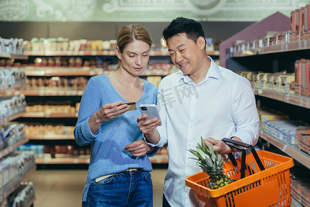 男女的手摄影照片_多元化的家庭夫妇亚洲男女在超市满意和快乐的购物，使用手机上的应用程序选择产品和购物清单，使用信用卡