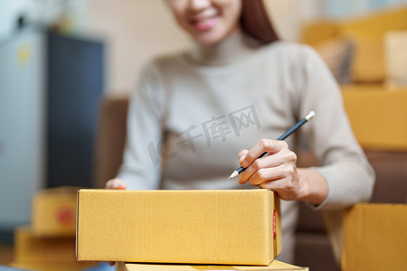 一家小型初创公司和中小企业主（一位亚洲女性企业家）正在将信息写在盒子上以整理产品，然后将其装入内盒中供客户使用