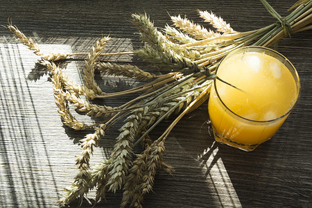 阳光下木桌上鲜榨的黄色果汁和成熟小麦的小穗。
