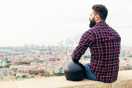 坐着背摄影照片_留着胡子的男人戴着头盔坐着看城市