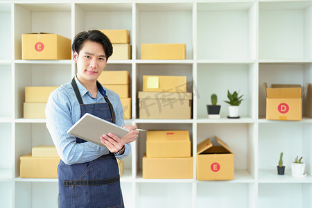 一家小型初创企业和中小企业主的肖像，一位亚洲男性企业家检查订单以整理产品，然后将其装入内盒供客户使用