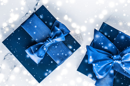 平铺摄影照片_冬季节日礼盒，配有蓝色丝绸蝴蝶结、大理石背景上的雪花，作为豪华美容品牌的圣诞和新年礼物，平铺设计