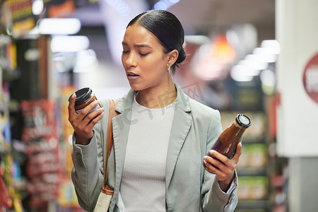 超市标签摄影照片_在商店或超市购物、零售和顾客，阅读选择的产品标签来决定或比较酱汁瓶。