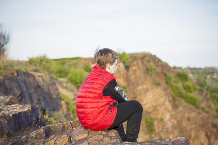 一个孩子坐在悬崖顶上，观察下面发生的事情。