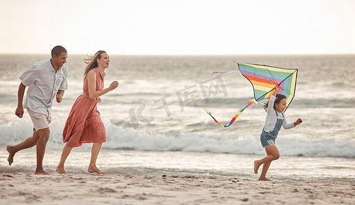 杆子上的风筝摄影照片_幸福的家庭，海滩度假，孩子和父母一起在海边跑步时放风筝。