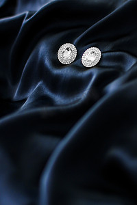 蓝色礼物摄影照片_深蓝色丝绸背景的豪华钻石耳环，节日魅力珠宝礼物