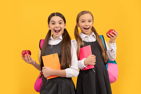 穿着校服的快乐孩子拿着书和苹果，健康吃校餐、零食