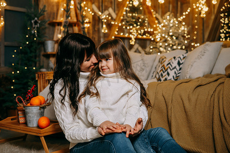 家庭环境摄影照片_一个小女孩和她的母亲在圣诞树旁边的沙发上享受舒适的家庭环境。