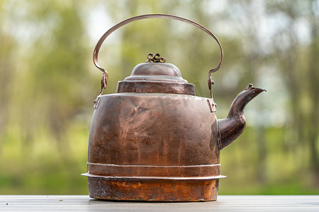 木桌上的旧铜水壶，背景是树木