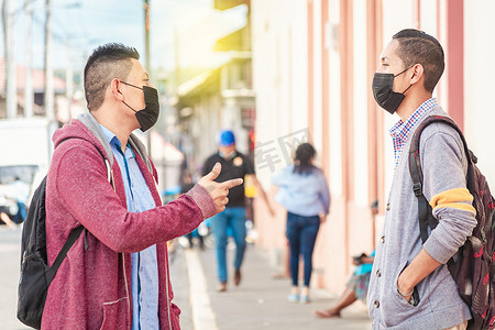戴口罩的男人摄影照片_两个戴面具的年轻人在户外交谈，两个戴面具的朋友进行交谈，对话概念和社交距离