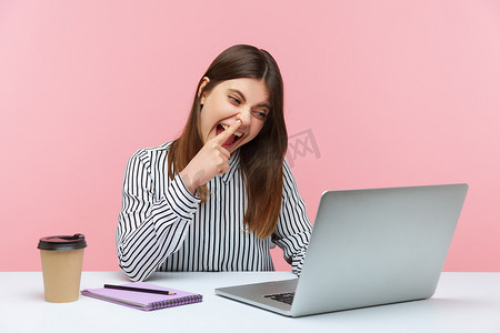 疯狂工作摄影照片_情绪化的年轻女性坐在粉红色背景的办公室里工作。