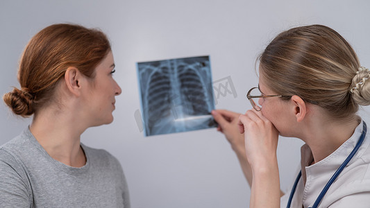 骨骼检查摄影照片_医生会诊一位白人妇女并对肺部 X 光检查做出评论。