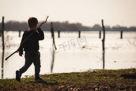 冬天拿着大棍子在湖边行走的小男孩