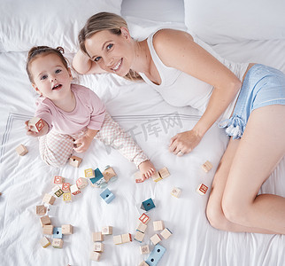 快乐宝贝摄影照片_快乐的妈妈，婴儿在床上，从上面玩有趣的教育玩具。
