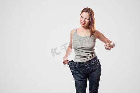 穿着大牛仔裤和灰色上衣的年轻女子快乐美丽的细腰肖像，显示减肥成功