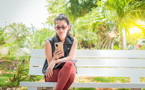 坐在长凳上查看手机的女孩，坐在公园里用手机发短信的快乐女人，坐在长凳上发送短信的女人