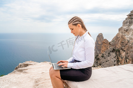 一位女士坐在露台上用 MacBook 键盘打字，可以看到美丽的海景。