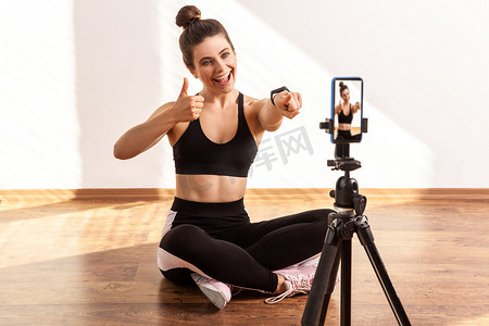 赞扬摄影照片_快乐的健身教练指着手机摄像头竖起大拇指，赞扬你的在线锻炼
