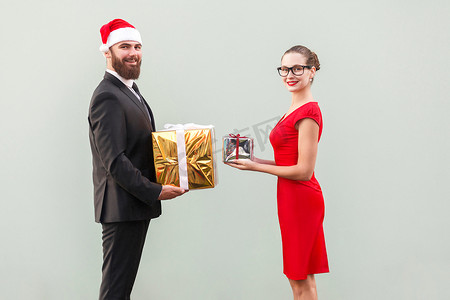 商务馈赠摄影照片_一对夫妇带着露齿微笑看着相机，并互相赠送礼品盒，以纪念圣诞节。