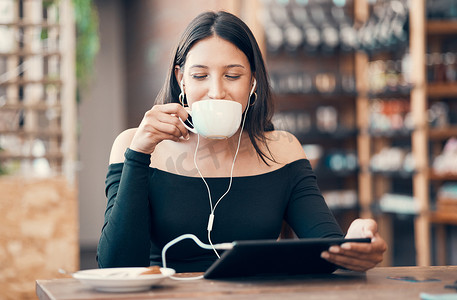 美丽、快乐、轻松的学生，拿着平板电脑在咖啡馆里喝咖啡，用耳机听播客和音乐。