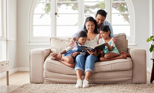 母亲读书摄影照片_年轻快乐的家庭坐在沙发上，一起在家里读书，同时放松。