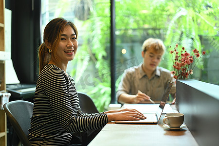 自信的女性网站开发人员与同事坐在现代办公室里，对着镜头微笑