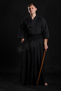 日本和服摄影照片_穿着传统日本和服的剑道大师正在黑色工作室背景下用竹剑练习武术。