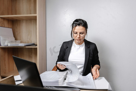 一位女士坐在办公室办公桌前记笔记的图片。