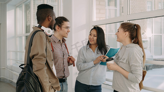 四名多民族学生站在大学宽敞的白色大厅里，以积极的方式互相交谈。