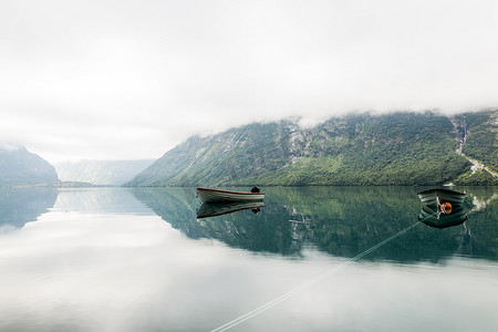 小船背景摄影照片_孤独的小船平静的湖面，有薄雾的山背景