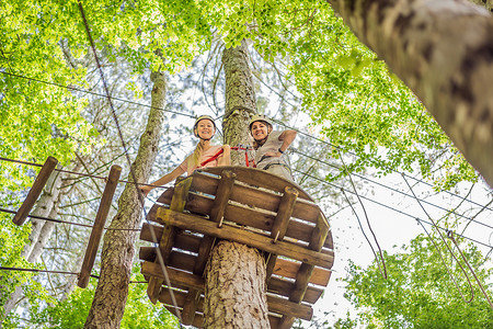 两名女女孩在森林中的极端公路电车滑索中滑翔攀登，在树上的登山绳安全链接上到树顶绳索冒险公园。