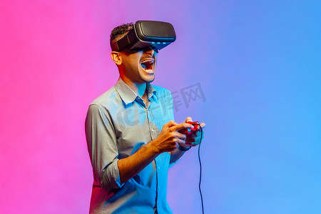 玩电子游戏摄影照片_戴着 VR 眼镜的男人玩电子游戏，使用模拟器进行教育，情绪激动地大喊大叫。
