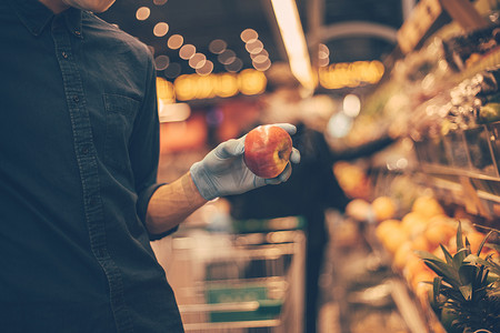 戴着防护口罩的男子在超市挑选苹果时。