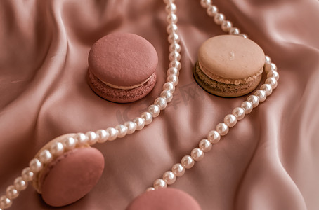 丝绸背景上的甜马卡龙和珍珠首饰、巴黎别致珠宝、法式甜点食品和豪华糖果品牌的蛋糕马卡龙、节日礼物