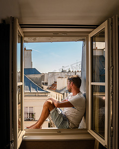 法国的卧室摄影照片_年轻人坐在窗前，眺望巴黎这座城市。