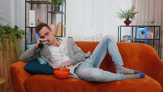 男人躺在沙发上吃薯条，在家看有趣的电视连续剧、在线足球比赛