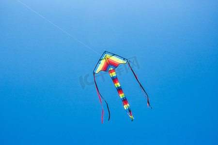 一只色彩缤纷的风筝在清澈的蓝天上飞翔，长尾巴和彩带