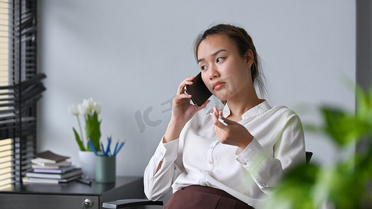 亚洲女员工在现代办公室工作，进行手机通话