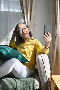 微笑的中年妇女拿着智能手机与朋友或亲戚进行视频通话，在家享受愉快的交谈
