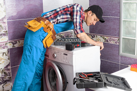 水管三通摄影照片_工人水管工在洗衣房修理洗衣机。
